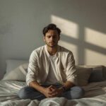 Homem sentado na cama com expressão pensativa, refletindo sobre sua vida sexual.